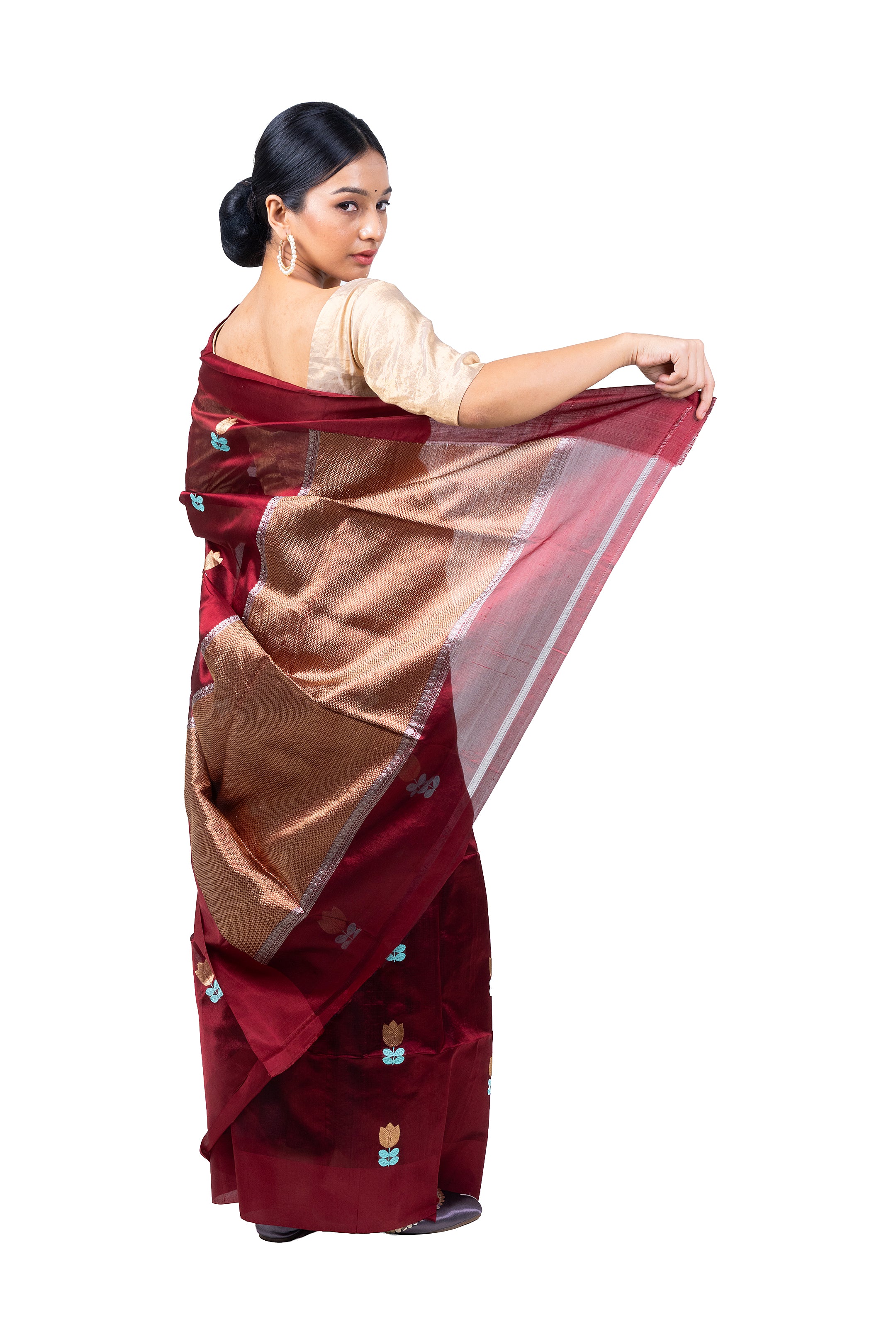 Woman wearing a traditional maroon saree with a gold border on a white background