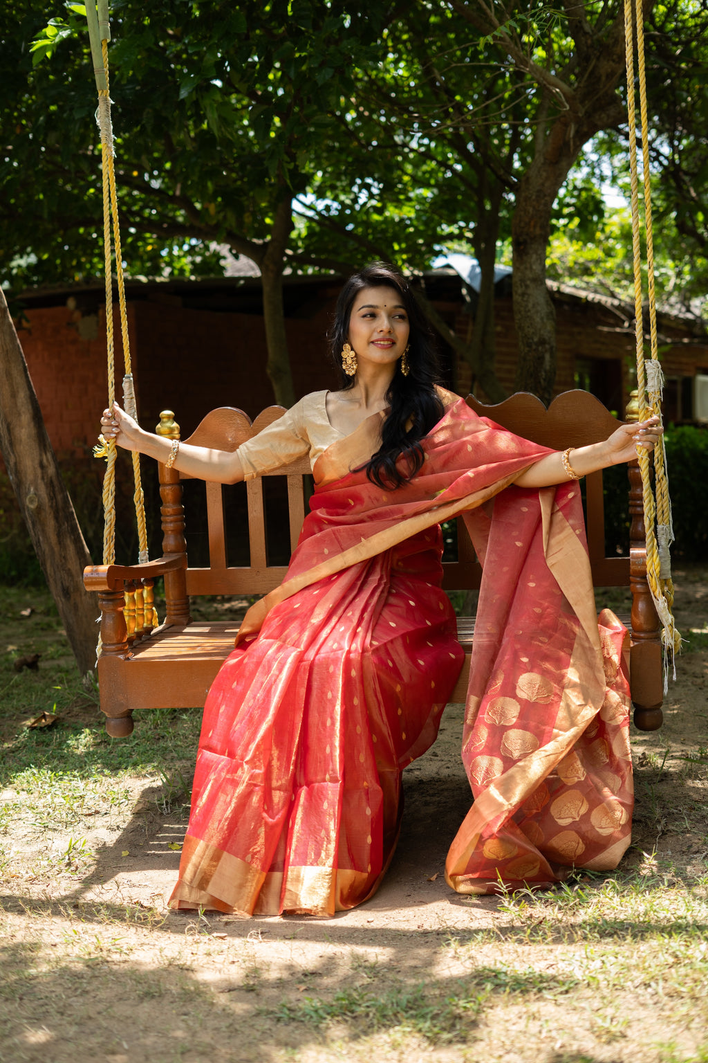 Woman in a red saree sitting on a wooden swing outdoors