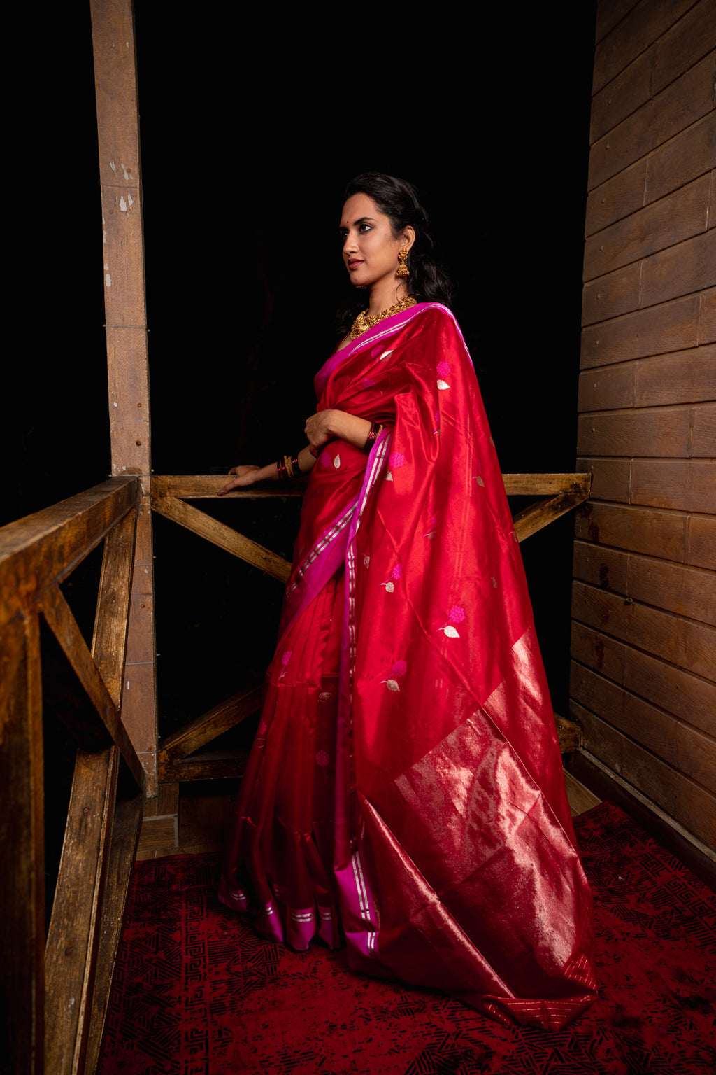 Woman in a red saree standing on a wooden platform at night.