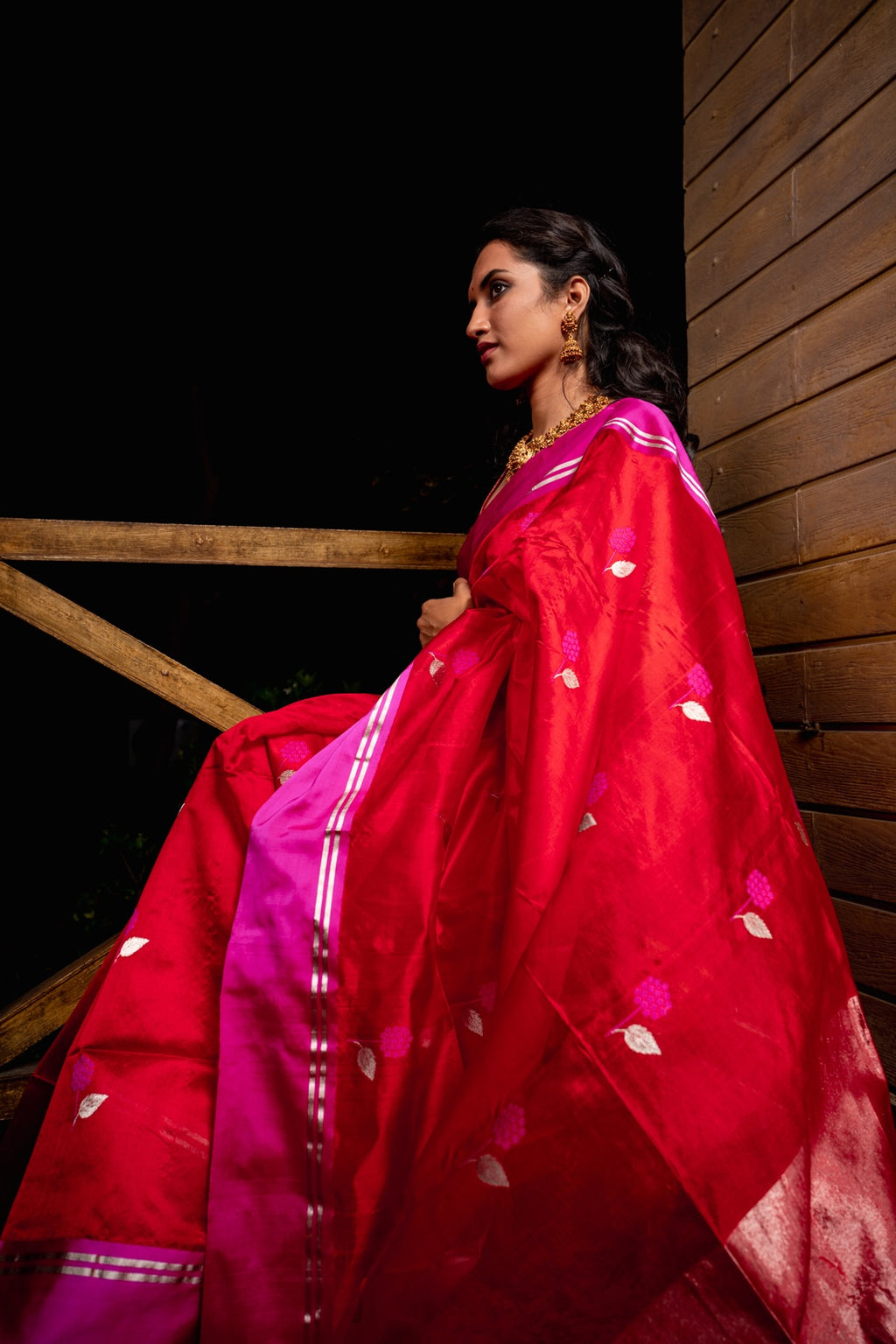 Woman wearing a red saree with pink blouse against a dark background