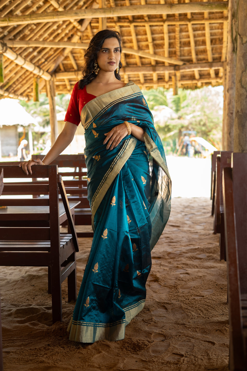 Woman in a blue saree with gold border standing in a rustic setting